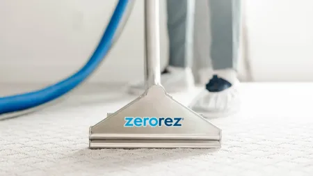 Close-up of Zerorez carpet cleaning tool on light carpet with blue hose in background.