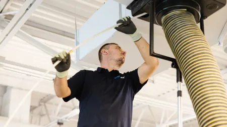 Technician inspecting and maintaining industrial air ventilation system with duct and flexible hose overhead